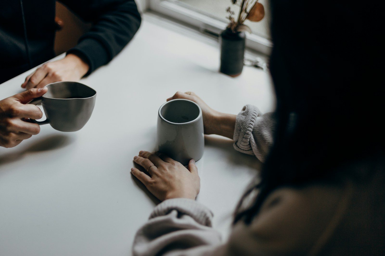 two people holding gray mugs at table